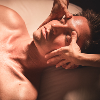 Man relaxes into a facial massage as therapist applies gentle pressure to the area above his eyes