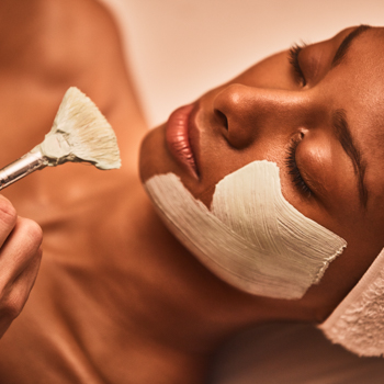 Woman's face with the first few strokes of a facial mask applied to her cheek and jawline