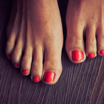 Freshly painted toenails brighten a woman's feet on a warm, wood-grain floor