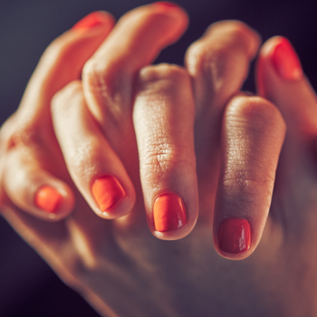 Hands clasped together with fingers entwined show a woman's freshly polished nails