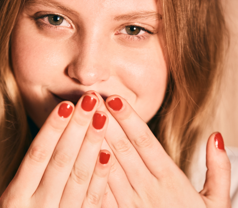 Woman smiles behind the fingers of her two hands as if suppressing a giggle