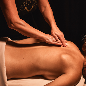 Massage therapist's hands smooth aching muscles between a woman's shoulder blades during a relaxing massage
