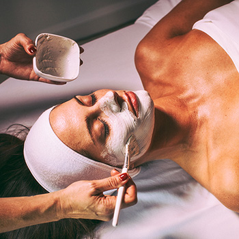 A woman with her eyes closed lying face-up while receiving an anti-aging facial treatment.