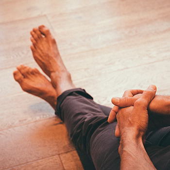 Man sitting with clasped hands and crossed, bare feet after a manicure and pedicure.