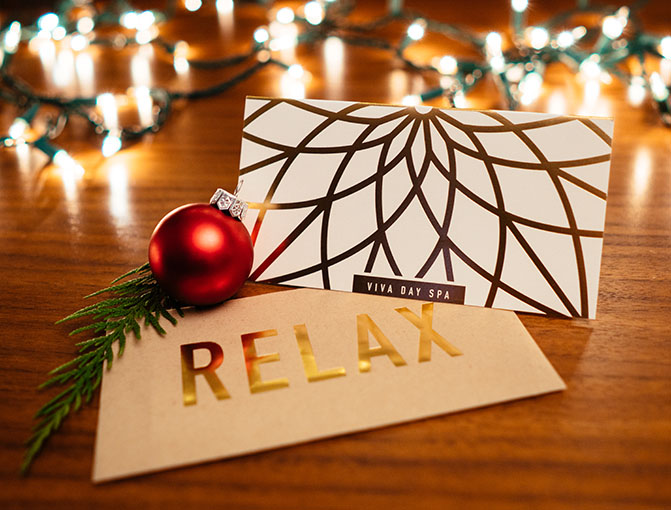 Viva Day Spa gift card and "relax" envelope on a table surrounded by Christmas lights, holly and a red ornament.