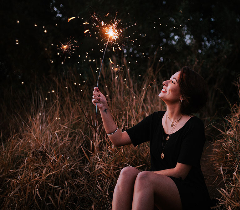 Woman holding a sparkler and looking up at it on New Year's Eve.