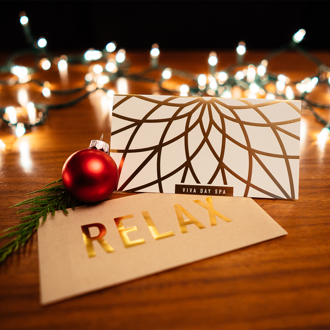 Viva Day Spa + Med Spa gift certificate on table with red Christmas ornament and holiday lights.