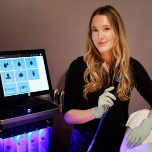 Viva Day Spa + Med Spa esthetician sitting in front of a Hydrafacial machine, holding the treatment wand.
