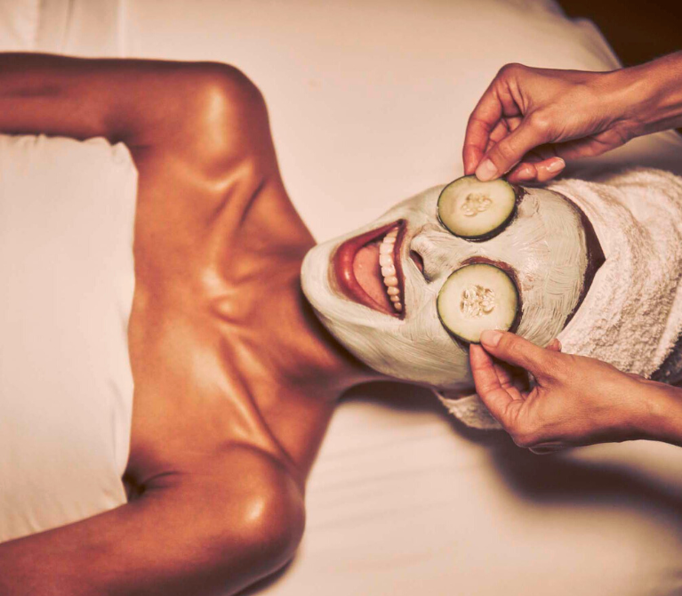 An esthetician placing cucumbers on the eyes of a woman receiving a facial treatment.