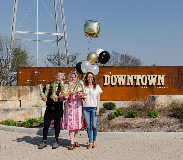 Viva Day Spa + Med Spa owners standing in front of a main sign in downtown Round Rock, Texas announcing the opening of Viva Round Rock in summer 2023.