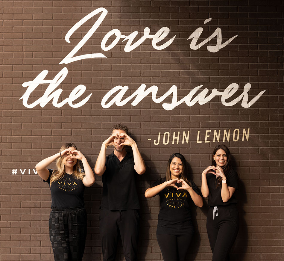 A group of four staff members of Viva Day Spa + Med Spa standing in front of Viva's "Love Is The Answer" mural at Domain Northside in Austin, Texas.
