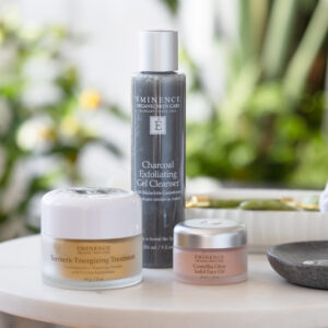 Eminence Organics skin care products sitting on a table, including Charcoal Exfoliating Gel Cleanser, Tumeric Energizing Treatment, and Camilla Glow Solid Face Oil